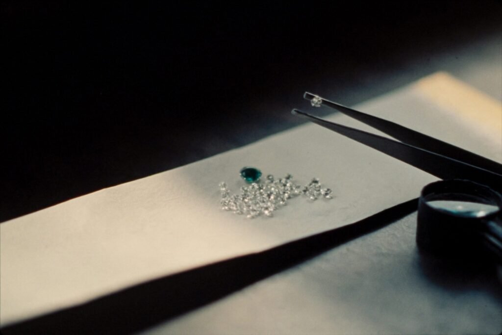 Loose diamonds and an emerald on a paper parcel with tweezers and a loupe