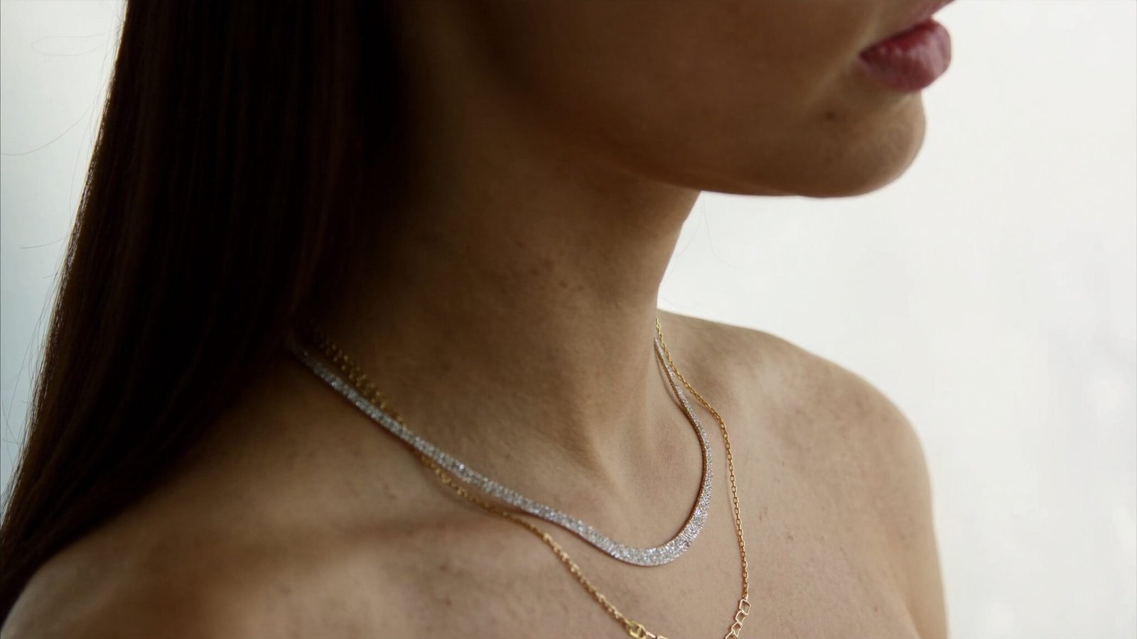 A woman wearing a diamond riviera necklace and a fine gold chain, shot in warm daylight