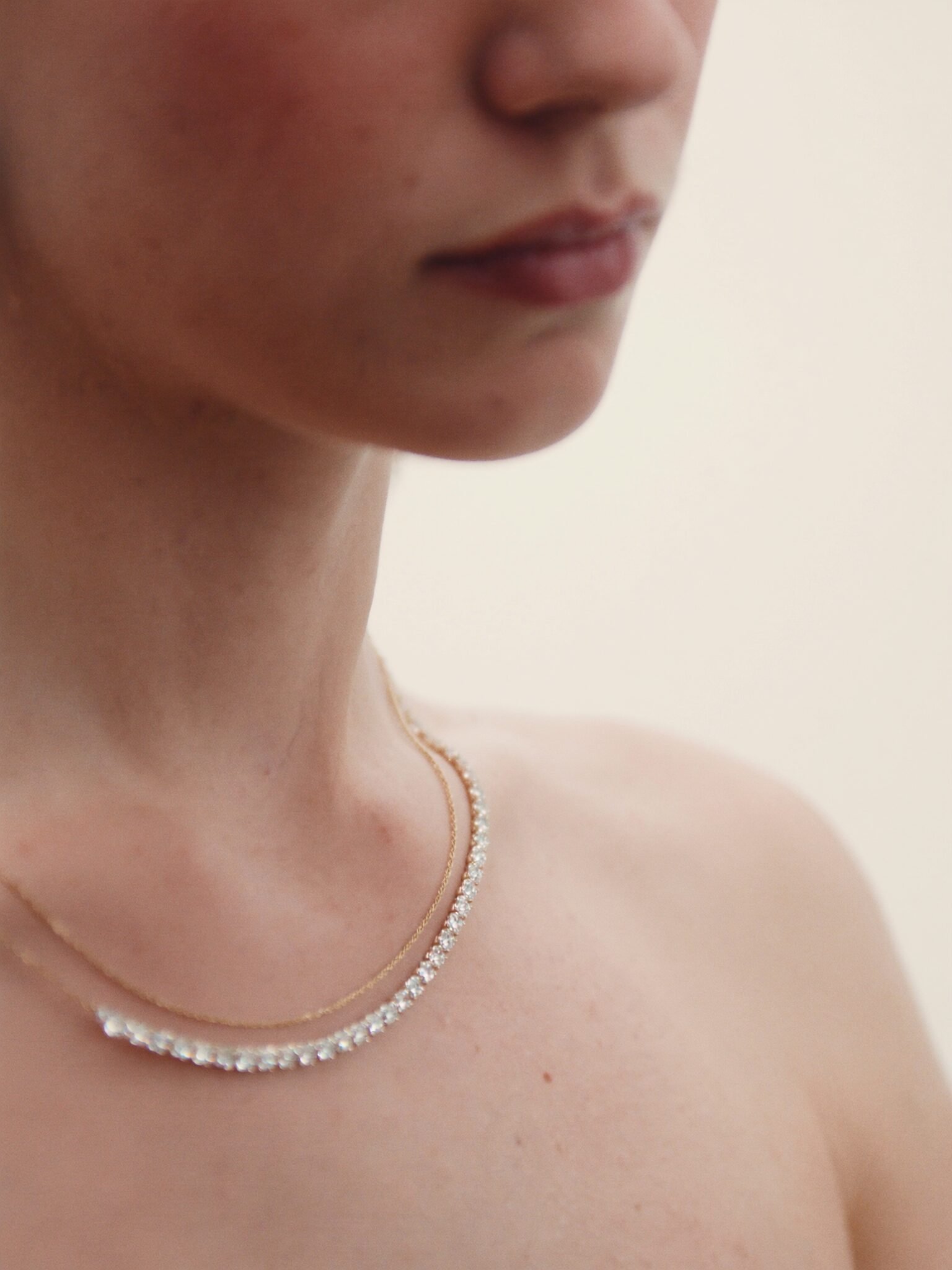 Portrait crop of a woman wearing a diamond riviera necklace and a fine gold chain