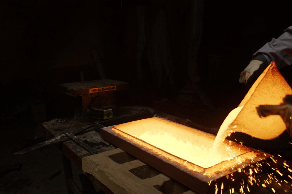 A goldsmith pouring molten gold into an ingot mould in a dark workshop