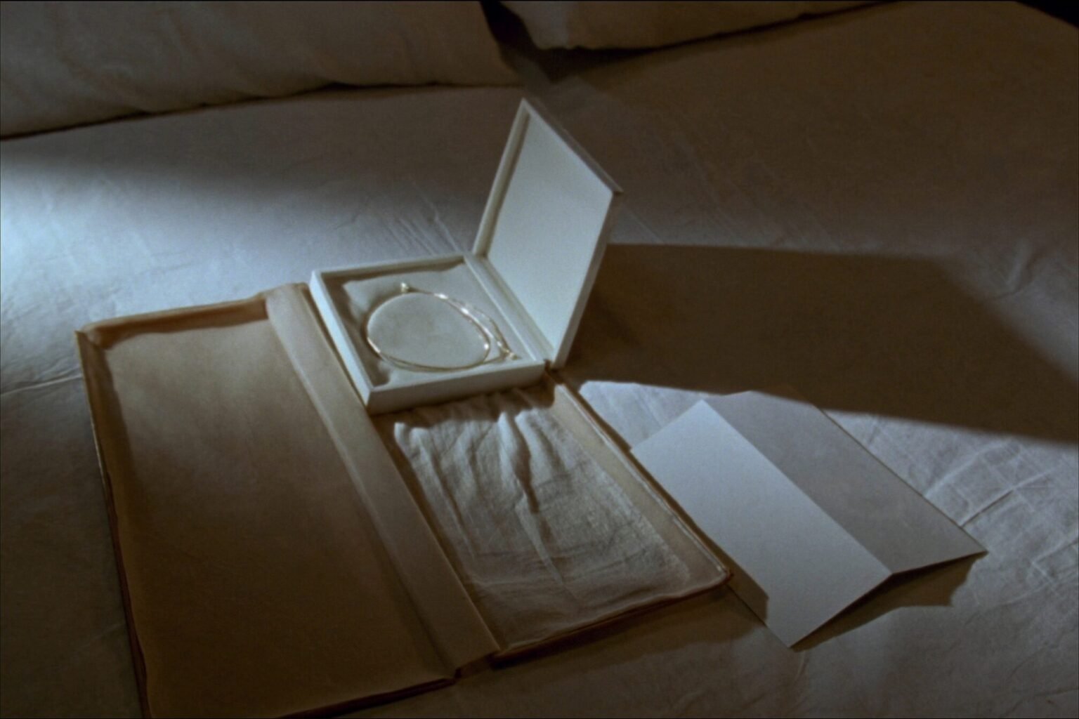 An open cream suede jewellery box on linen with a fine gold chain necklace inside